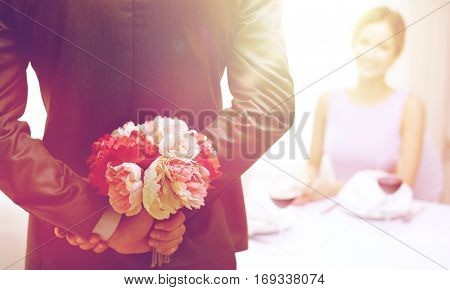 restaurant, people, celebration and holiday concept - close up of man hiding flowers behind from woman at restaurant