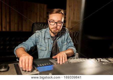 music, technology, people and equipment concept - man at mixing console in sound recording studio