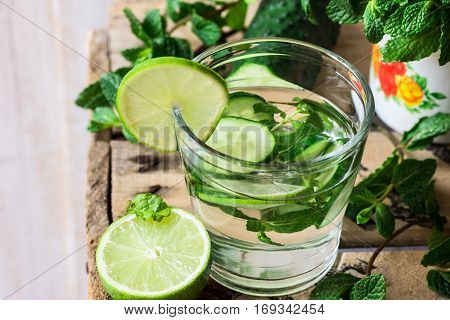 Close up of glass with detox cucumber water with fresh mint and lime on barn wood box, ingredients, spring or summer, outdoors, top angle view