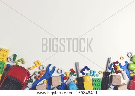 Colorful kids toys frame. Plastic toy construction tools, bolts, nuts, car, blocks, cubes on white background as frame with copy space for text. Flat lay. Top view. Toned picture