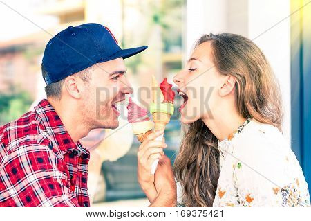 Young couple face to face eating ice cream in playful attitude - Attractive friends looking at each other having fun at bar cafe gelateria - Concept of teenagers romantic love moment -