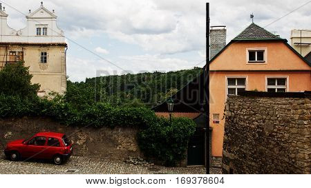 An old european town street with worn and rusty houses and walls and a red car