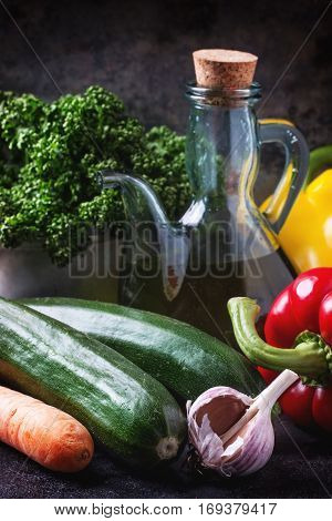 Vegetables and parsley with olive oil in glass bottle over dark background