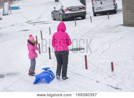 DNEPR UKRAINE - DECEMBER 03 2016:Mother with daughter getting ready to sledge on a snowy street in Dnepr, Ukraine at December 03, 2016