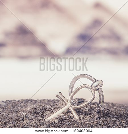 The Egyptian ankh is a cross in the sand against the backdrop of the Great Pyramids. Photo toned.