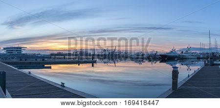 First rays of sun peeking over the horizon. Port twilight in the Valencia harbor cranes working loading transport ships, red and blue skyline reflected in water. gigapan