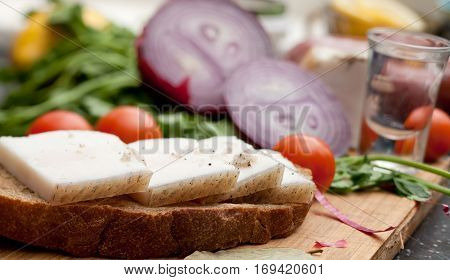 Lard on bread tomatoes onions fresh herbs and vodka on the table