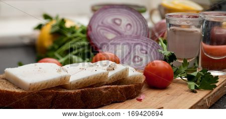 Lard on bread tomatoes onions fresh herbs and vodka on the table