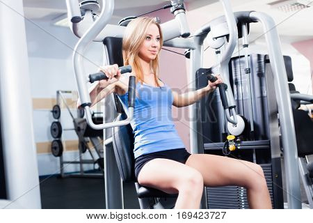Pretty Caucasian smiling woman is working out on butterfly machine. Young Bodybuilder Doing Exercise For Chest In The Gym.