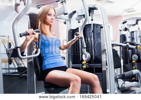 Pretty Caucasian smiling woman is working out on butterfly machine. Young Bodybuilder Doing Exercise For Chest In The Gym.