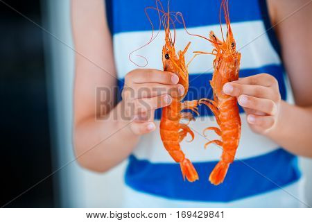 Close up of kid hands with cooked large shrimps