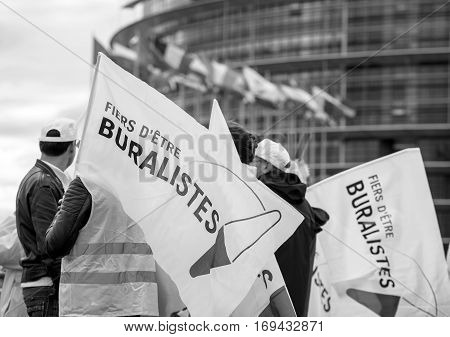 STRASBOURG FRANCE - OCT 7 2015: Rear view of tobacconists buralistes people protesting in front of the European Parliament building with flags placards while President Francois Hollande is entering the Parliament gates Confederation des buralistes