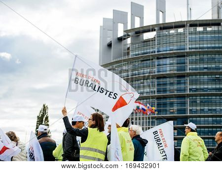 STRASBOURG FRANCE - OCT 7 2015: Rear view of tobacconists buralistes people protesting in front of the European Parliament building with flags placards while President Francois Hollande is entering the Parliament gates Confederation des buralistes