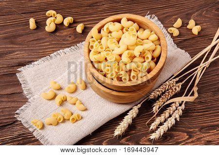 Raw elbow macaroni and rye ears in a wooden bowl on the table top view