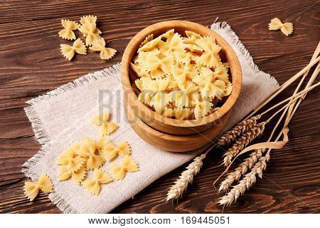 Pasta farfalle and rye ears in a wooden bowl on the table top view