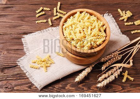 Raw pasta rotini and rye ears in a wooden bowl on the table top view