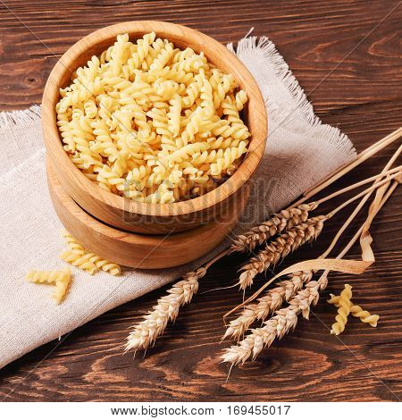 Raw pasta rotini and rye ears in a wooden bowl on the table