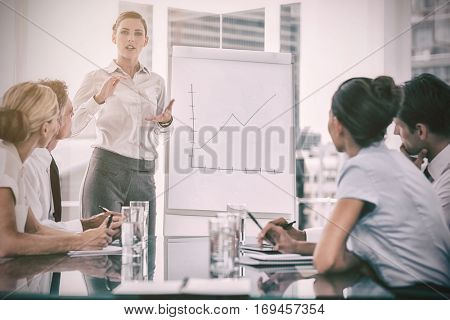 Businesswoman giving explication in front of a growing chart on a whiteboard during a meeting