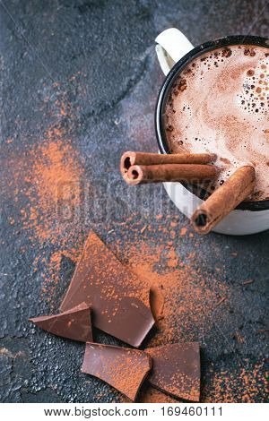 Vintage mug of hot chocolate with cinnamon sticks over dark background. Top view.