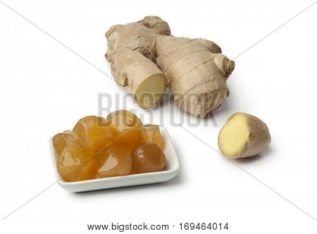Dish with stem ginger in syrup and fresh gingerroot on white background