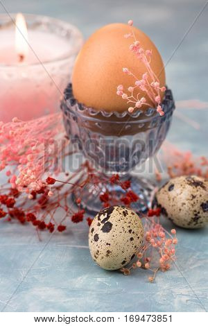 Easter egg in crystal cup scattered quail eggs spring red and pink small flowers burning candle in the background decorationtable settingelegant