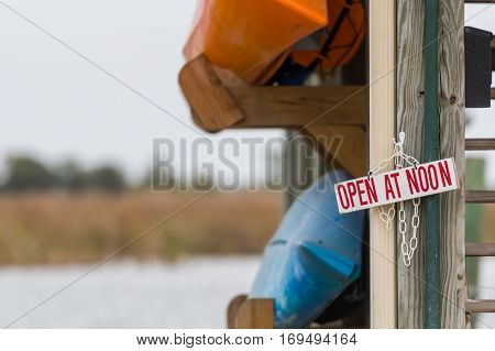 Open at Noon Sign with Two Kayaks hanging on ramp