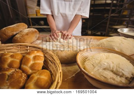 Mid-section of female baker kneading a dough in bakery shop