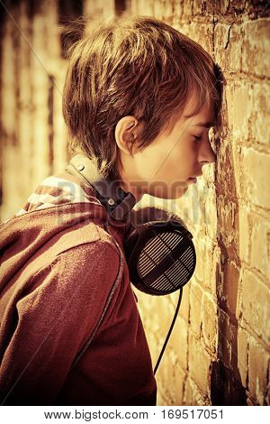 Teen boy standing in the street, turned away to face the wall. Sadness, depression. Teenage problems.