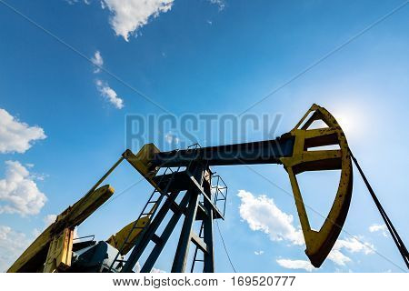Oil field with pump jack, profiled on blue sky with white clouds, on a sunny day in spring