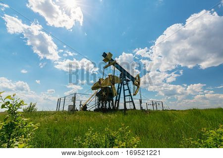 Oil field with pump jack, profiled on blue sky with white clouds, on a sunny day in spring