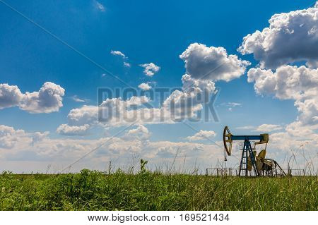 Oil field with pump jack, profiled on blue sky with white clouds, on a sunny day in spring