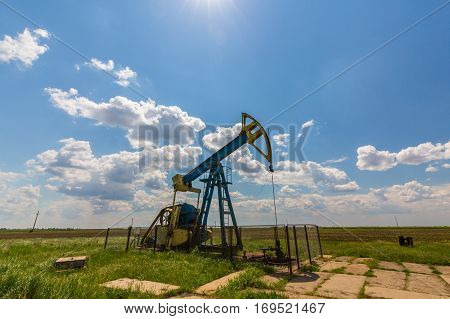 Oil field with pump jack, profiled on blue sky with white clouds, on a sunny day in spring