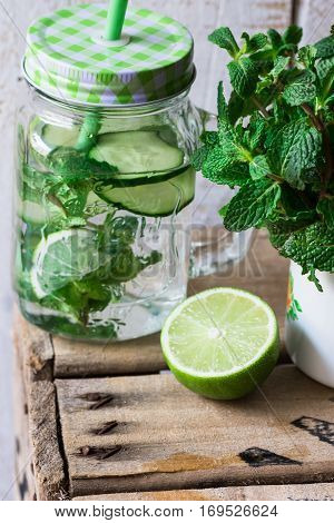 Mason jar mug with infused detox cucumber water with lime and mint ingredients wood box spring outdoors cleansing