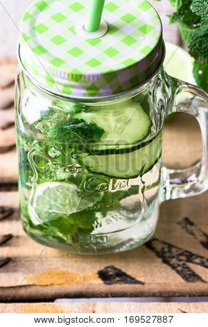 Jar mug with refreshing detox cucumber water with fresh mint and lime wood background outdoors spring cleansing