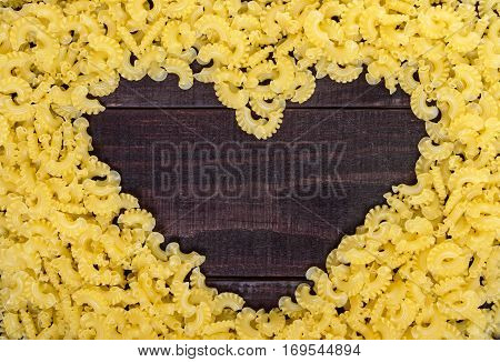 Raw macaroni - pasta Galetti. In the middle of the empty space in the shape of a heart on a dark wooden background.