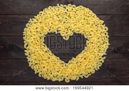 Raw macaroni - pasta Galetti. In the middle of the empty space in the shape of a heart on a dark wooden background.