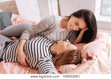 Perfect view. Two beautiful emotional loving women spending their free time at home and lying on a big cozy bed looking in each other eyes