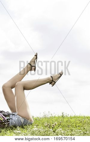 Low section of woman with feet up lying on grass against sky