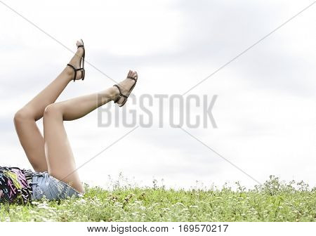 Low section of woman with feet up lying on grass against sky