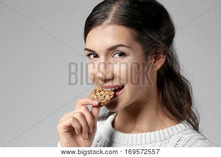 Pretty young woman eating tasty cookie, on grey background