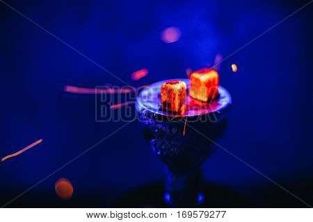 Hot coals on the bowl of the hookah with sparks for a traditional Eastern relaxation and enjoyment on a blue blurred background