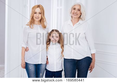 Full of gladness. ositive content smiling little girl and her mother and grandmother embracign and expressing joy at home