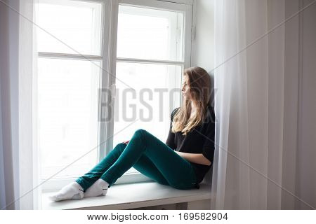 beautiful girl sitting at home in front of a window and dreams