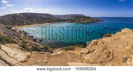 Malta - Panoramic view of Ghajn Tuffieha sandy beach with sail boat blue sky and crystal clear green sea water