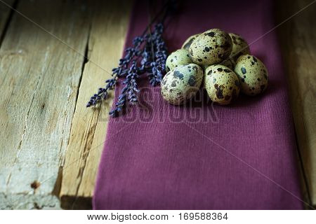 Quail eggs and lavender twigs on a lilac linen cloth on barn wood background, Easter, rustic vintage style, kinfolk, simplicity, close up
