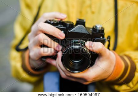 A young guy hipster, holding oldschool film camera, day outdoors, close up, center frame, ready to take a photo, soft-focus
