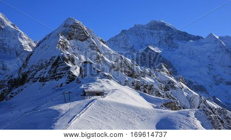 Winter scene in Grindelwald Swiss Alps. Snow covered mountains Lauberhorn and Jungfrau summit station of a cable car.