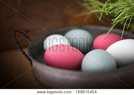 Close up of pastel colored easter eggs in a bowl on a wooden table