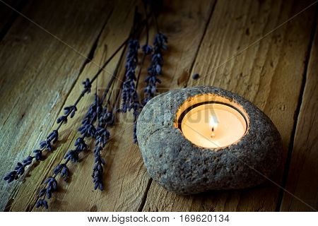 Stone candle holder with tea light on aged wood background, lavender twigs, Easter, peace and tranquility concept, kinfolk