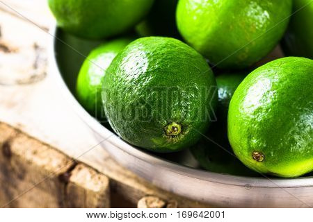 Heap of ripe colorful limes in aluminum dish on wood box, sunlight, freshness, health concept, detox drink ingredient